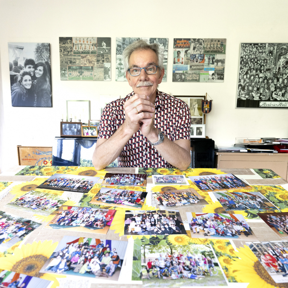 Oud-leraar Maarten Bijveld poseert achter een tafel vol met klassenfoto's van zijn oud leerlingen.