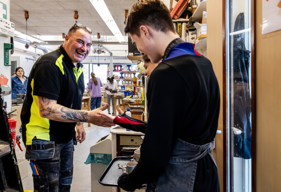 Docent John Schouten neemt lachend koffie in ontvangst van leerlingen.